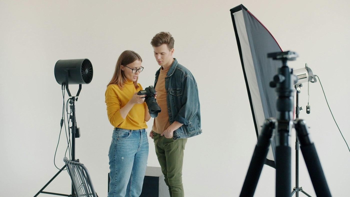 Two people reviewing photos on a camera in a bright studio